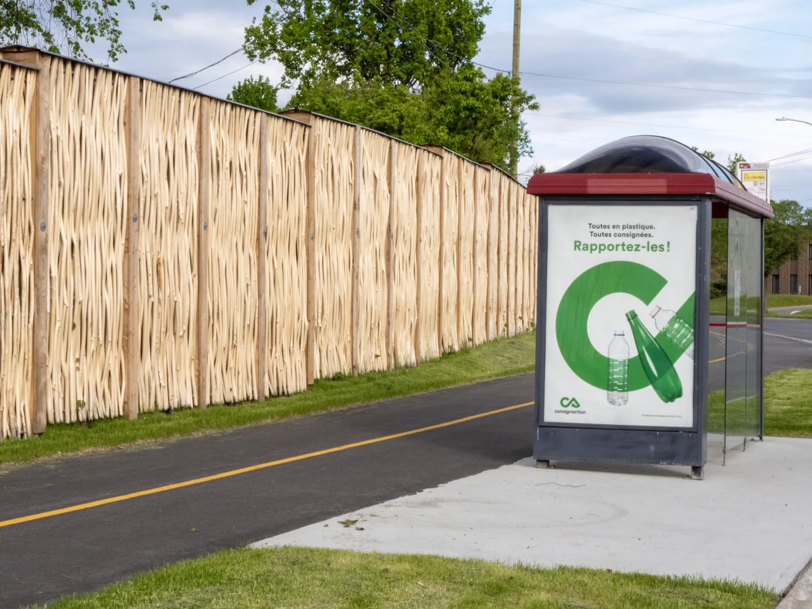 Pilebyg® noise barrier in debarked willow with a bike path and bus shelter in Boucherville