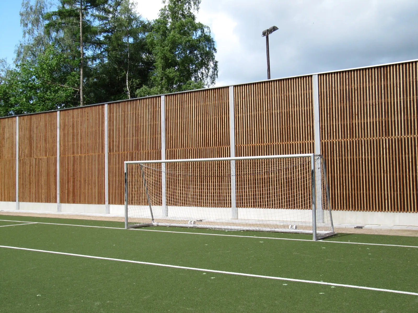 HF1 larch-wood noise barrier surrounding a sports field