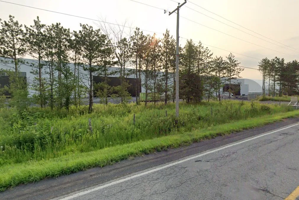 Compo-Haut-Richelieu site in July 2023, with sparse vegetation and buildings visible from the road